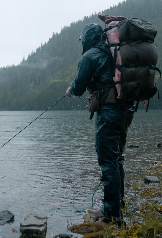 Person with a large backpack pulling a boat to shore and forested mountains in the background